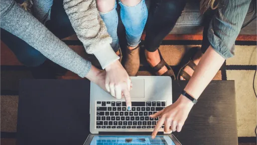 Three people sitting on a couch pointing at a laptop.
