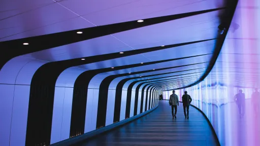 Twee personen lopen door een futuristische, paars verlichte gang.