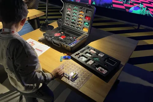 Kind bekijkt robotica-onderdelen op een tafel met een open koffer vol elektronische componenten.