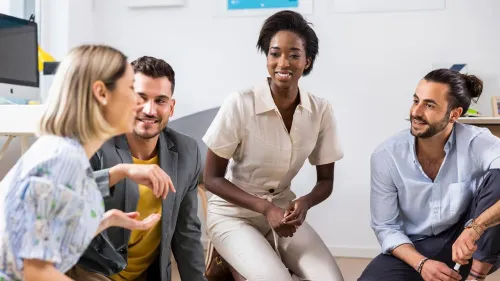 Vier mensen praten en lachen samen in een lichte kantoorruimte.