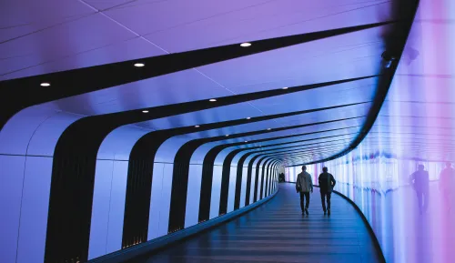 Twee mensen lopen door een futuristische, kleurrijk verlichte tunnel.